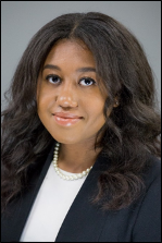 A close up headshot of a young woman in a blue blazer